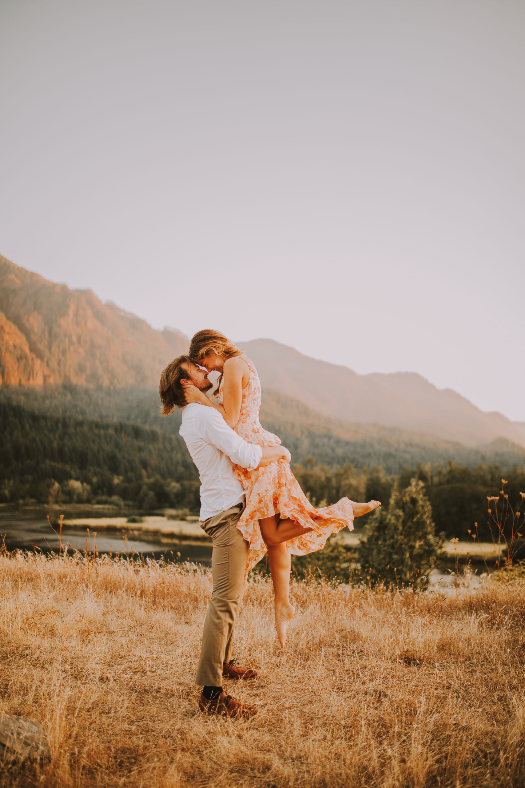 The groom lifts his bride into the air for an intimate kiss during their sunset engagement session at Columbia River Gorge in Portland, Oregon
