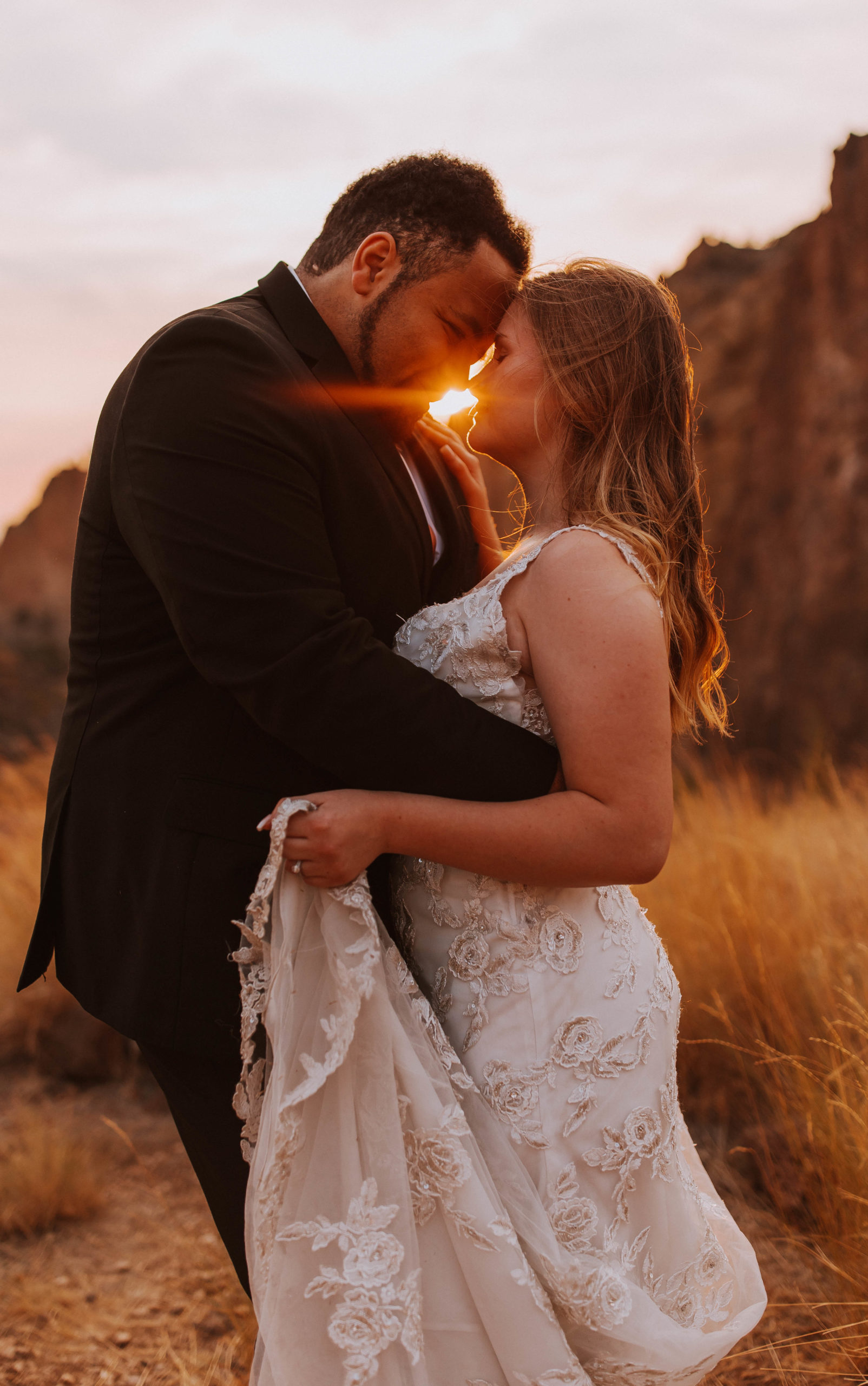 The bride and groom lean in to share a kiss during golden hour in front of the sun as it shine through the brides hair