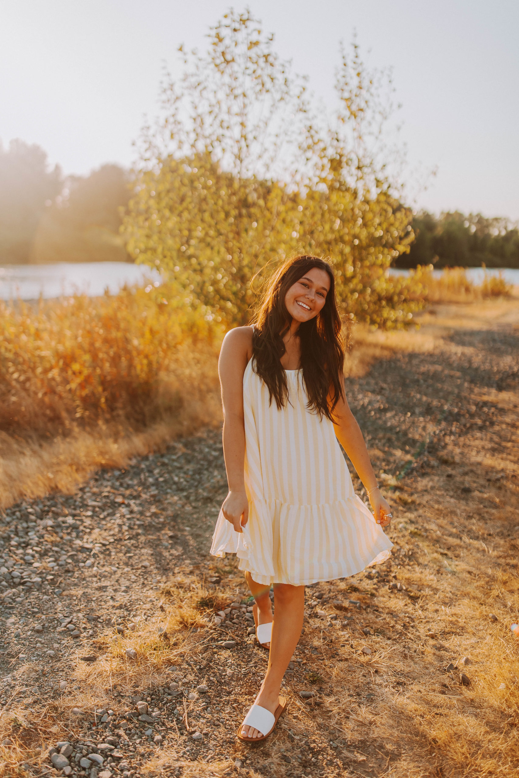 senior smiling with her sundress flowing in the wind during golden hour