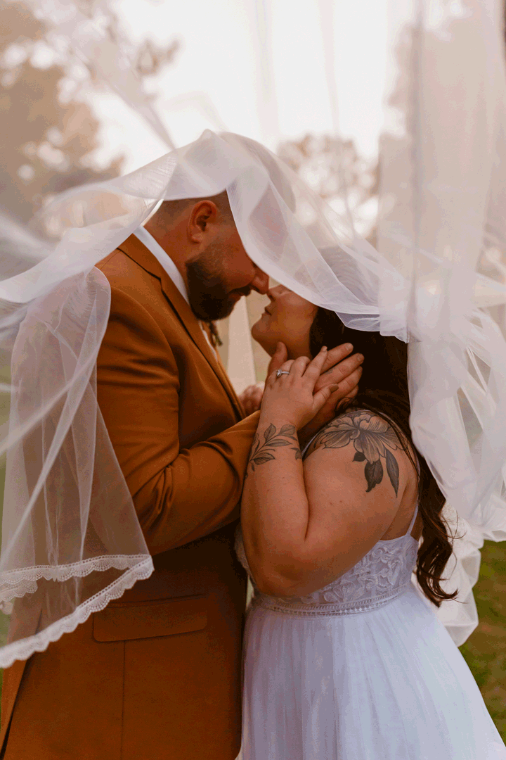 bride and groom lean in for a kiss underneath their wedding veil