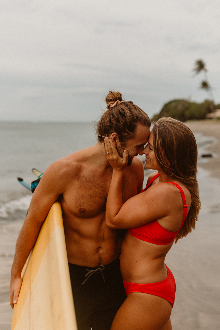 Cute fit couple kissing on the beach with their surf board in Maui Hawaii